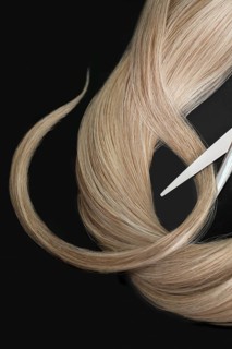 A strand of blond hair with scissors on a black background. Close-up
