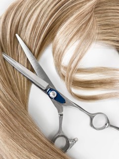 A strand of blond hair with scissors on a white background. Close-up