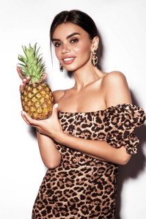 Beautiful sexy woman with pineapple in hands in a leopard dress and earrings