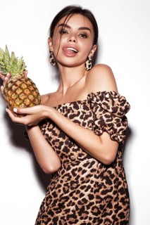 Beautiful sexy woman with pineapple in hands in a leopard dress and earrings