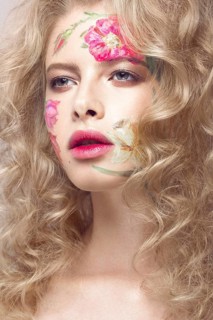 Beautiful blond girl with tresses and a floral pattern on the face. Beauty flowers. Portrait shot in studio