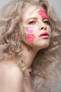Beautiful blond girl with tresses and a floral pattern on the face. Beauty flowers. Portrait shot in studio