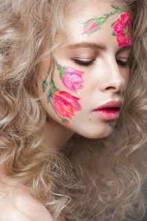 Beautiful blond girl with tresses and a floral pattern on the face. Beauty flowers. Portrait shot in studio