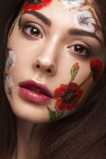 Beautiful brunette girl with curls and a floral pattern on the face. Beauty flowers. Portrait shot in studio