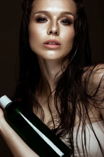 Beautiful girl with a bright make-up and wet hair and skin with bottle of cosmetic products in the hands. Beauty face. Picture taken in the studio on a black background
