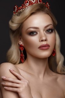 Beautiful blond girl with a golden crown and earrings and professional evening make-up. Beauty face. Picture taken in the studio