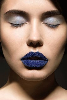 Portrait of beautiful girl with unusual blue lips and eyes closed. Picture taken in the studio on a gray background