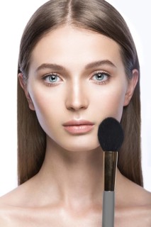 Beautiful young girl with a light natural make-up and beauty tools in hand. Picture taken in the studio on a white background