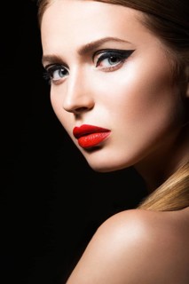 Beautiful young girl with a bright make-up and red nails. Picture taken in the studio on a black background