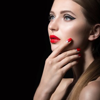 Beautiful young girl with a bright make-up and red nails. Picture taken in the studio on a black background