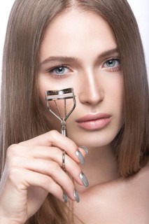Beautiful young girl with a light natural make-up and beauty tools in hand. Picture taken in the studio on a white background