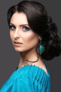 Beautiful girl in a blue dress with evening make-up and hairstyle. Beauty face. Picture taken in the studio on a black background. Hairstyle back view