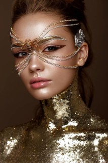 Beautiful girl in a golden mask and bright evening make-up. Beauty face. Photo taken in studio