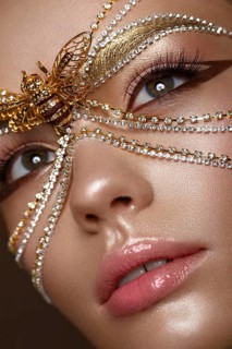 Beautiful girl in a golden mask and bright evening make-up. Beauty face. Photo taken in studio