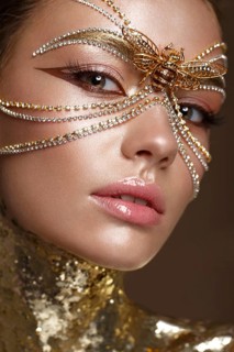 Beautiful girl in a golden mask and bright evening make-up. Beauty face. Photo taken in studio