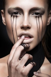 Beautiful girl with creative make-up in Gothic style and the threads of eyes. Art beauty face. Picture taken in the studio on a black background
