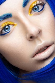 Beautiful girl in a bright blue wig in the style of cosplay and creative makeup. Beauty face. Art image. Picture taken in the studio on a yellow background