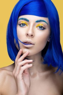 Beautiful girl in a bright blue wig in the style of cosplay and creative makeup. Beauty face. Art image. Picture taken in the studio on a yellow background