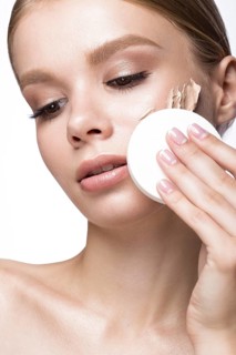 Beautiful young girl with sponge for application make-up and French manicure. Beauty face. Picture taken in the studio on a white background