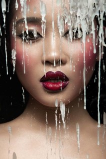 Beautiful Asian girl with bright make-up behind glass with drops of wax. Beauty face. Picture taken in the studio on a black background