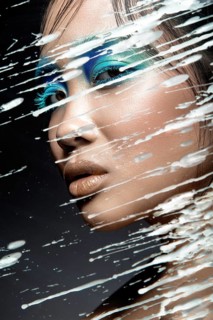 Beautiful Asian girl with bright blue make-up behind glass with drops of wax. Beauty face. Picture taken in the studio on a black background