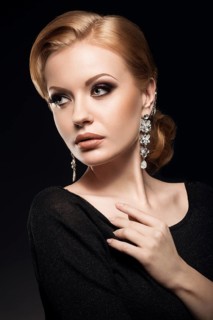 Beautiful red-haired girl in a black dress with a smooth evening haircut in the form of waves and bright makeup. Beauty face. Picture taken in the studio on a black background