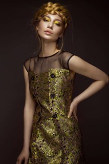 Beautiful girl in a gold dress with creative makeup and braids on her head. The beauty of the face. Photos shot in the studio