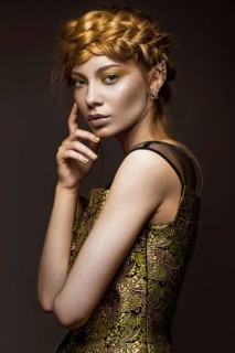 Beautiful girl in a gold dress with creative makeup and braids on her head. The beauty of the face. Photos shot in the studio
