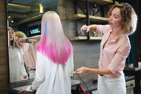 Beautiful blond girl with colored pink hair in a hairdressing salon. The client looks at herself in the mirror