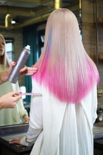 Beautiful blond girl with colored pink hair in a hairdressing salon. The client looks at herself in the mirror