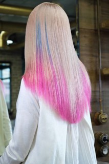 Beautiful blond girl with colored pink hair in a hairdressing salon. The client looks at herself in the mirror