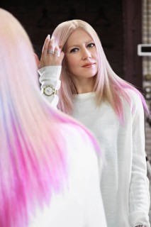 Beautiful blond girl with colored pink hair in a hairdressing salon. The client looks at herself in the mirror