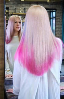 Beautiful blond girl with colored pink hair in a hairdressing salon. The client looks at herself in the mirror