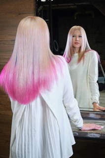Beautiful blond girl with colored pink hair in a hairdressing salon. The client looks at herself in the mirror