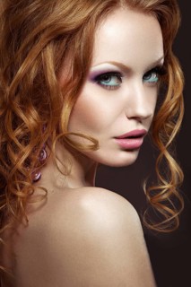 Beautiful red-haired girl with bright makeup and curls. Picture taken in the studio on a black background