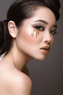 Beautiful girl with oriental type evening hair and makeup. Portrait shot in the studio on a gray background