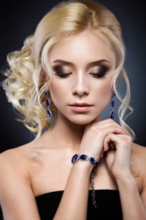 Beautiful blond girl in a black dress with evening haircut in the form of waves and bright makeup. Beauty face. Picture taken in the studio