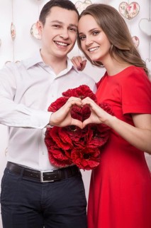 Beautiful young couple in love with a bouquet of flowers showing the form of heart hands. Valentine's Day. Picture taken in the studio