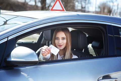 Joyful girl driving a training car with a drivers license card in her hands