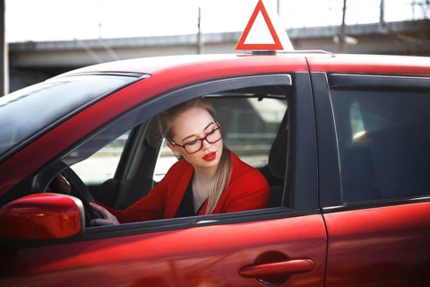 Young beautiful happy woman in red sitting at the wheel new training car