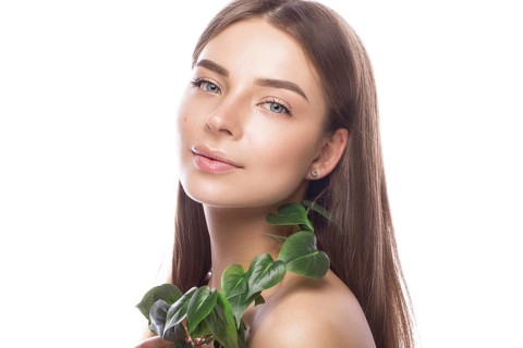 Beautiful young girl with a light natural make-up and perfect skin with Green branch in her hand. Beauty face. Picture taken in the studio on a white background