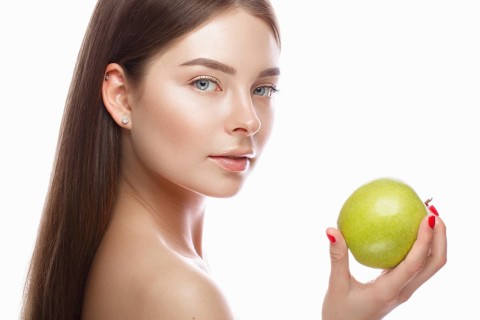 Beautiful young girl with a light natural make-up and perfect skin with apple in her hand. Beauty face. Picture taken in the studio on a white background