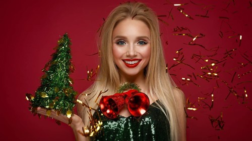 Beautiful blonde girl in a New Year's image with Christmas bells around her neck and green tree. Beauty face with festive makeup. Photo taken in the studio