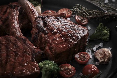 Piece of appetizing pork steak on the bone with vegetables in vintage style