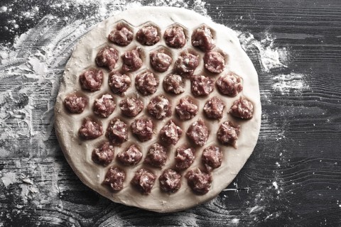 Handmade homemade dumplings on a metal tray on a wooden background with flour. Diy meat dumplings
