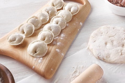 Handmade homemade dumplings on a wooden tray on a white plate with flour. Diy meat dumplings