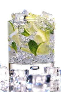 Glass of Mojito summer alcoholic cocktail with ice cubes mint and lime on white background with raw lime and mint leaf