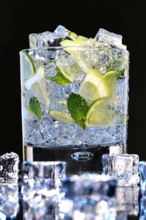 Glass of Mojito summer alcoholic cocktail with ice cubes mint and lime on black background with raw lime and mint leaf