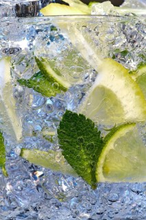 Glass of Mojito summer alcoholic cocktail with ice cubes mint and lime on white background with raw lime and mint leaf
