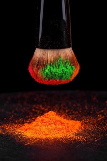 Cheek brush with neon cosmetic powder colorful pile and isolated on black background